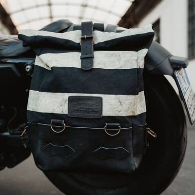 The Holy Freedom Folsom Bag is crafted from 60% cowhide and 40% cotton canvas, this bag combines rugged durability with classic style. The roll-top design offers flexibility and secure storage, while the striped canvas print adds a bold touch. Featuring adjustable leather shoulder straps, a sturdy leather handle with the Holy Freedom writing, and burnished metal hardware. Inside, you'll find a dedicated laptop pocket (fits up to 16 inches) and an internal zip pocket for your essentials. It includes anchors for easy attachment to your bike. With a capacity of 14-18 liters, this 100% handmade bag is ready for any journey. Elevate your adventures with the Holy Freedom Folsom bag!
